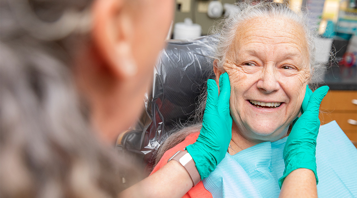 Business photography example. A dentist wearing teal gloves examines the teeth of a smiling senior patient.